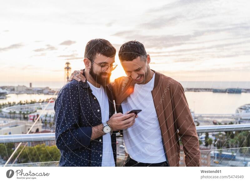 Schwules Ehepaar mit Handy auf dem Aussichtspunkt über der Stadt mit Blick auf den Hafen, Barcelona, Spanien Partner Partnerschaften Touristen Telekommunikation