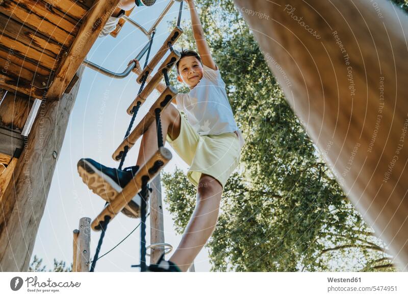 Junge klettert Leiter im öffentlichen Park an einem sonnigen Tag Farbaufnahme Farbe Farbfoto Farbphoto Außenaufnahme außen draußen im Freien Tageslichtaufnahme