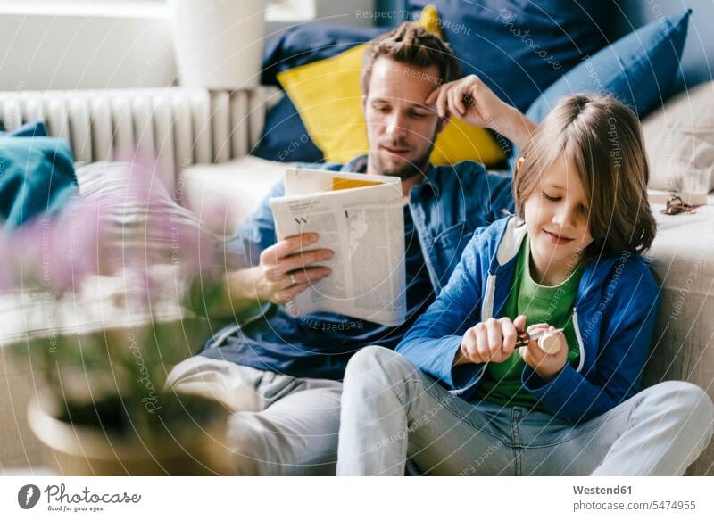 Vater liest Zeitung, während der Sohn zu Hause schnitzt Söhne Papas Väter Vati Vatis Papis Zuhause daheim schnitzen Zeitungen lesen Lektüre Kind Kinder Familie