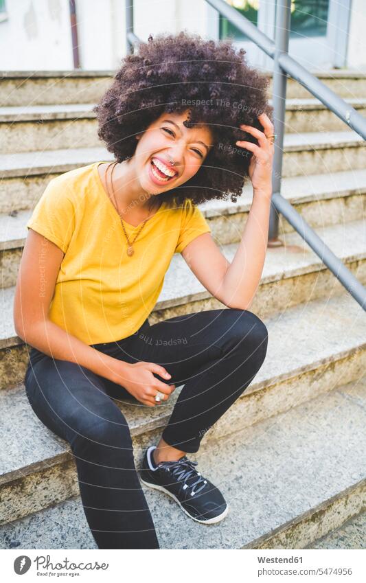 Porträt einer lachenden jungen Frau, die im Freien auf einer Treppe sitzt Leute Menschen People Person Personen gelockt gelockte Haare gelocktes Haar lockig