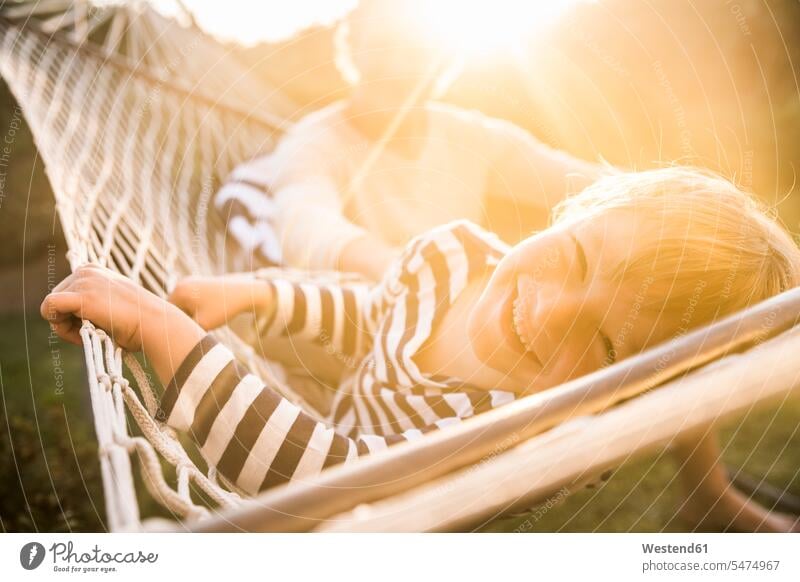 Porträt eines lächelnden Jungen in der Hängematte liegend mit dem Vater im Hintergrund Hängematten abends Jahreszeiten sommerlich Sommerzeit entspannen relaxen