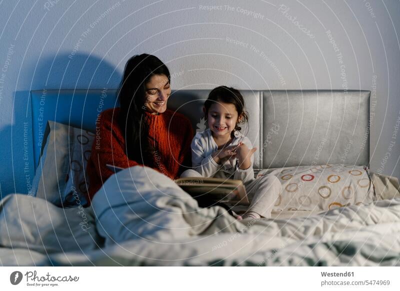 Glückliche Mutter und ihre kleine Tochter sitzen zusammen im Bett und schauen Bilderbuch Leute Menschen People Person Personen 2 2 Menschen 2 Personen zwei