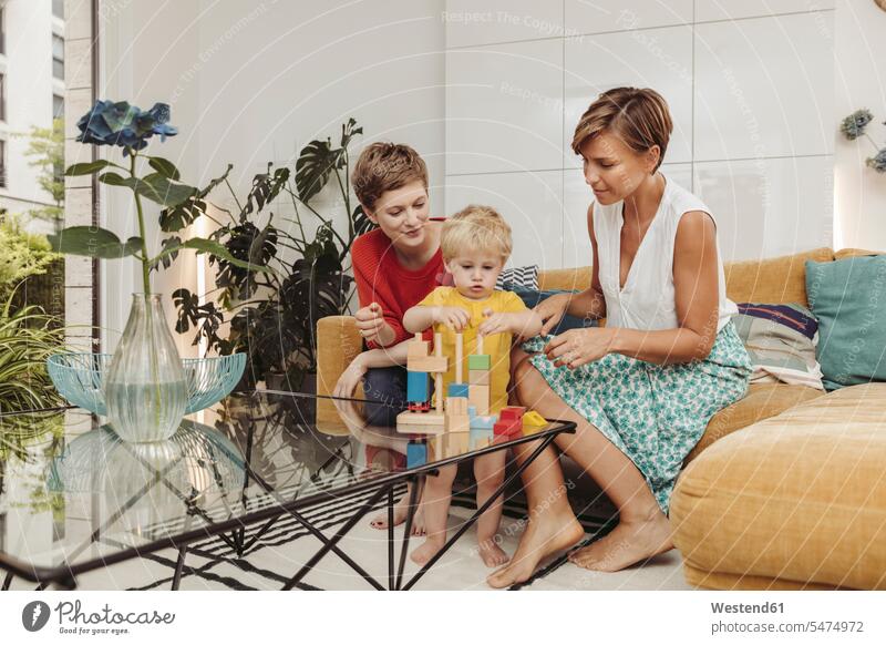 Zwei Mütter lernen und spielen mit ihrem Kind zu Hause lesbisch Mutter Zuhause Familie Mensch Eltern Holzspielzeug Freizeit Häusliches Leben sitzen Wohnzimmer