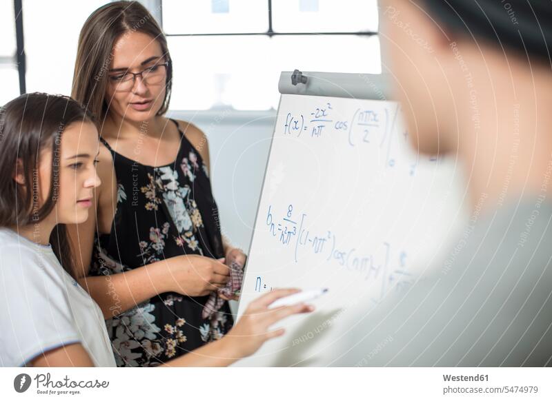 Lehrerin hilft Teenager-Mädchen beim Schreiben von Formeln an der Tafel Whiteboard Schule helfen Klassenzimmer schreiben Schulklasse Pädagoge Bildung