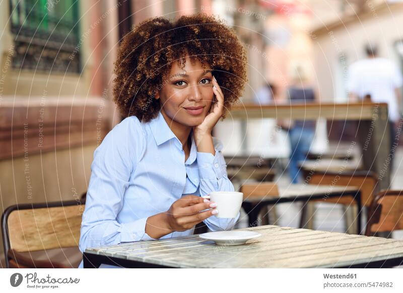Porträt einer lächelnden Frau mit Afro-Frisur, die im Freiluftcafé sitzt Afro-Look Afros Afrolook Portrait Porträts Portraits sitzen sitzend Cafe Kaffeehaus
