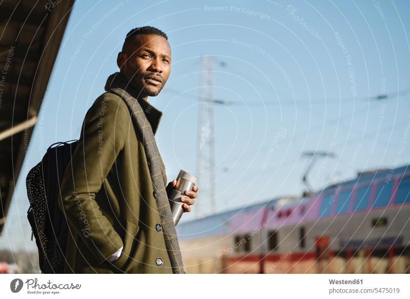 Stilvoller Mann mit wiederverwendbarem Becher wartet auf den Zug geschäftlich Geschäftsleben Geschäftswelt Geschäftsperson Geschäftspersonen Businessmann