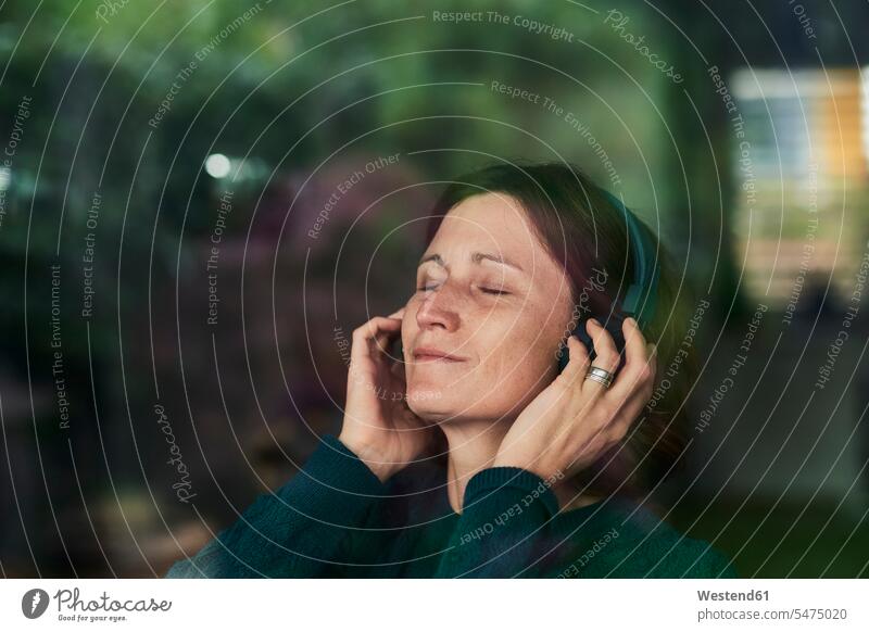Nahaufnahme einer Frau mit geschlossenen Augen, die zu Hause über Kopfhörer Musik hört Farbaufnahme Farbe Farbfoto Farbphoto Außenaufnahme außen draußen