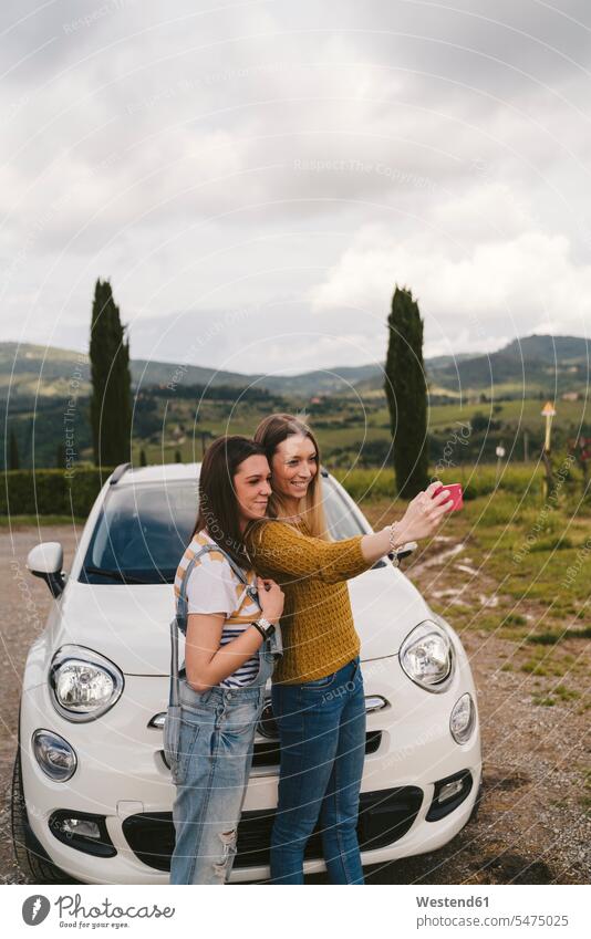 Zwei glückliche junge Frauen stehen neben einem Auto und machen ein Selfie, Toskana, Italien Leute Menschen People Person Personen Europäisch Kaukasier