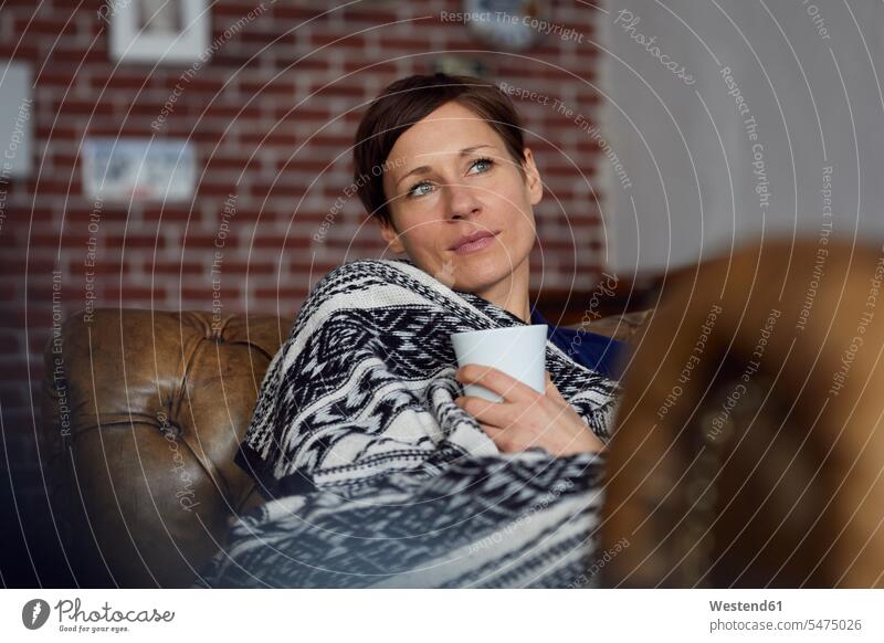 Frau auf Sofa, die sich zu Hause entspannt und Tee trinkt entspanntheit relaxt weiblich Frauen trinken Tees liegen liegend liegt tagträumen Tagtraum Couches