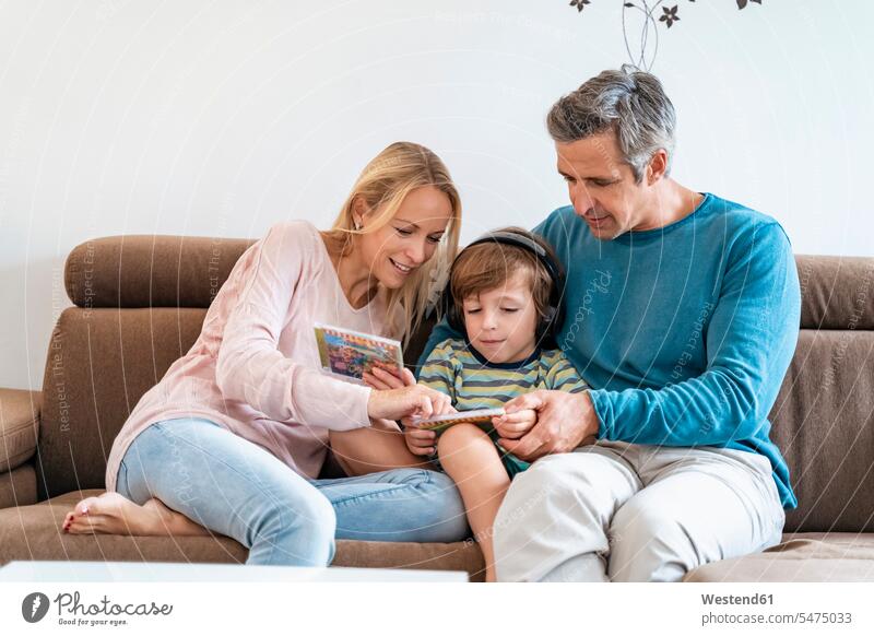 Familie zu Hause auf der Couch mit einem Jungen, der mit Kopfhörern Musik hört Couches Liege Sofas Kopfhoerer Medium CD ROM CD ROMs CD-ROM CD-ROMs CDs