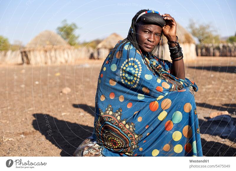 Porträt einer Muhacaona-Frau in ihrer traditionellen farbenfrohen Kleidung, Oncocua, Angola sitzend sitzt Farben Farbtoene Farbton Farbtöne farbig mehrfarbig