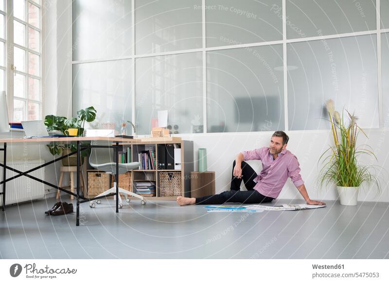 Lässiger Mann mit Plänen, der in einem Loft-Büro auf dem Boden sitzt Lofts sitzen sitzend leger Männer männlich Office Büros Böden Boeden Plan Erwachsener