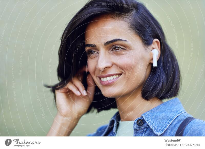 Nahaufnahme einer lächelnden Geschäftsfrau mit drahtlosen Kopfhörern an der Wand Farbaufnahme Farbe Farbfoto Farbphoto Deutschland Geschäftsfrauen Businessfrau
