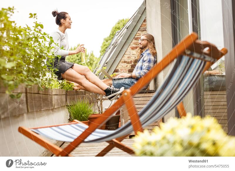 Junges Paar sitzt auf ihrem Balkon im Sommer, reden und mit Laptop Sommerzeit sommerlich Pflanze Pflanzenwelt Flora Websurfen Im Net surfen Surfen Balkone