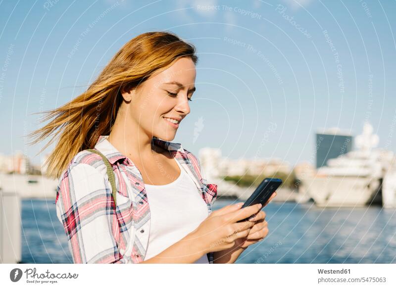 Textnachrichten von Frauen auf Smartphones, die an sonnigen Tagen am Meer stehen Farbaufnahme Farbe Farbfoto Farbphoto Außenaufnahme außen draußen im Freien