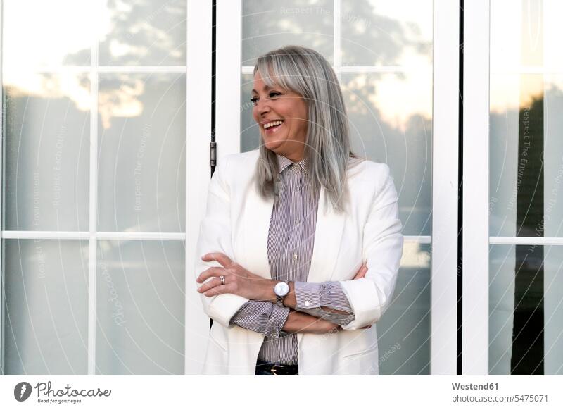Lächelnde berufstätige Frau steht mit verschränkten Armen da und schaut weg gegen die Bürotür Farbaufnahme Farbe Farbfoto Farbphoto Spanien Außenaufnahme außen