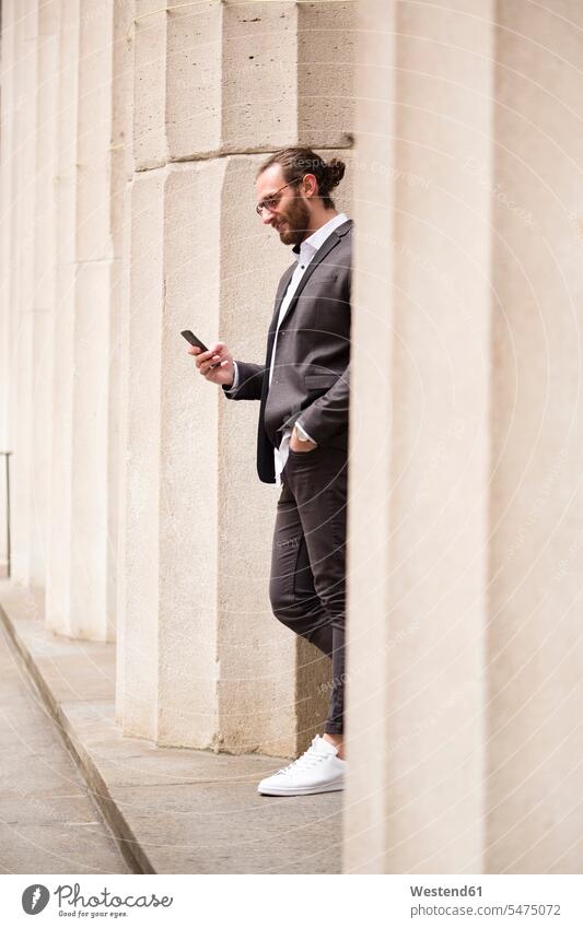 Junger Geschäftsmann steht zwischen den Säulen der Börse und schaut auf Handy, New York City, USA geschäftlich Geschäftsleben Geschäftswelt Geschäftsperson