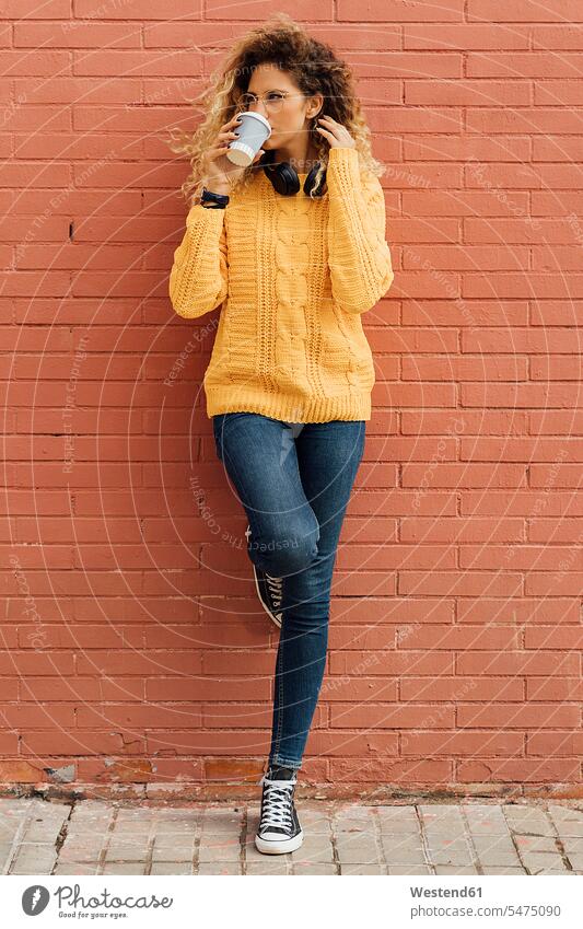 Schöne junge Frau schaut weg, während sie Kaffee aus einer Einwegtasse gegen eine rote Backsteinmauer trinkt Farbaufnahme Farbe Farbfoto Farbphoto Spanien