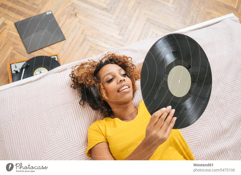 Junge Frau liegt auf dem Bett und hört Musik mit Kopfhörern und Plattenspieler Leute Menschen People Person Personen Alleinstehende Alleinstehender Singles