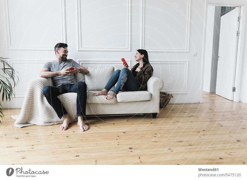 Paar sitzt zu Hause auf der Couch und benutzt seine Smartphones Europäer Kaukasier Europäisch kaukasisch sitzen sitzend dunkelhaarig dunkle Haare Wohnzimmer