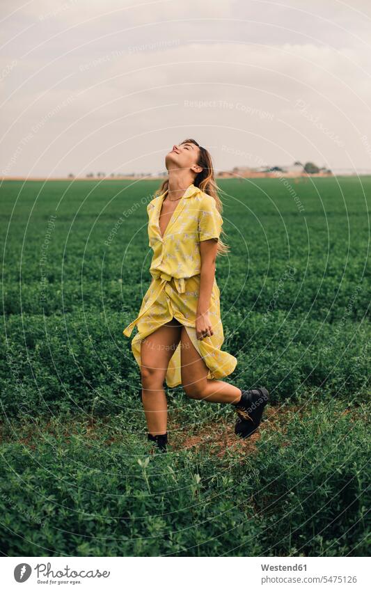Junge Frau zu Fuß in einem grünen Feld lächeln gehen gehend geht Kleid Kleider Sommer Sommerzeit sommerlich gelb gelber gelbes weiblich Frauen laufen rennen