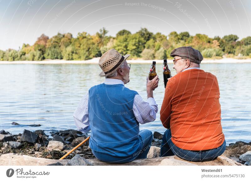 Alte Freunde sitzen am Flussufer und trinken Bier Rückansicht Rueckansicht Rückenansicht Rueckenansicht von hinten Bierflasche Bierflaschen Lebensqualität Pause