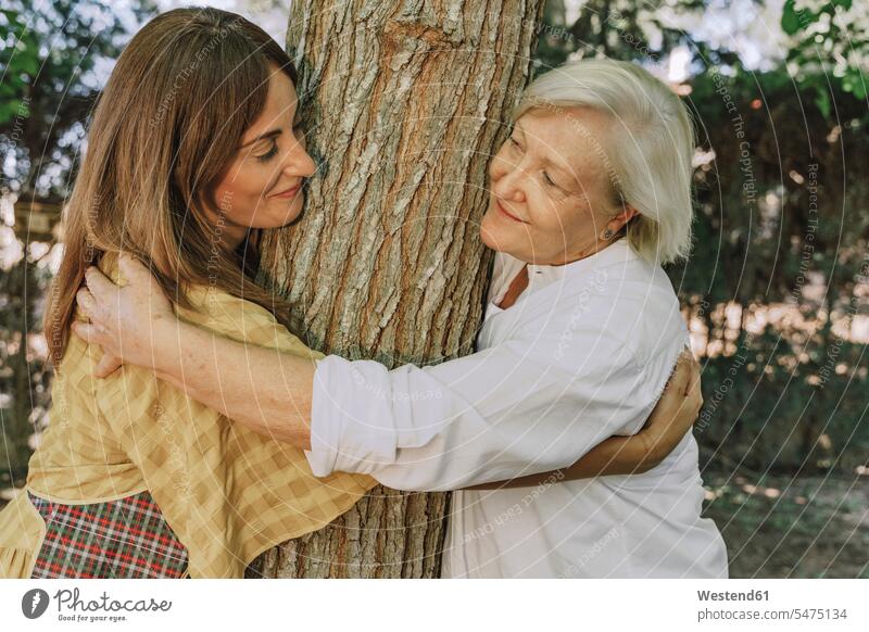 Mutter und Tochter sehen einander an, während sie im Hof einen Baumstamm umarmen Farbaufnahme Farbe Farbfoto Farbphoto Spanien Freizeitbeschäftigung Muße Zeit