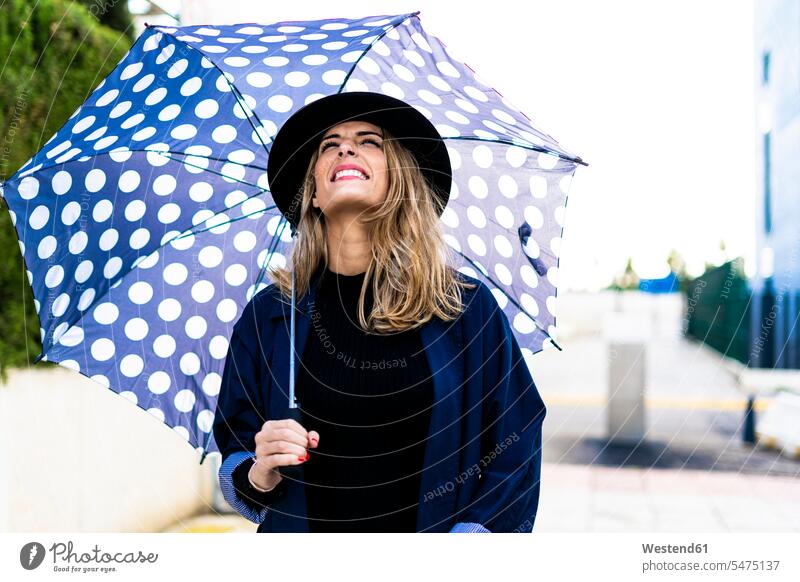 Blonde Frau mit Regenschirm an einem regnerischen Tag Hut Hüte Spaziergang regnen dunkelblau weiblich Frauen blond blonde Haare blondes Haar Regenschirme