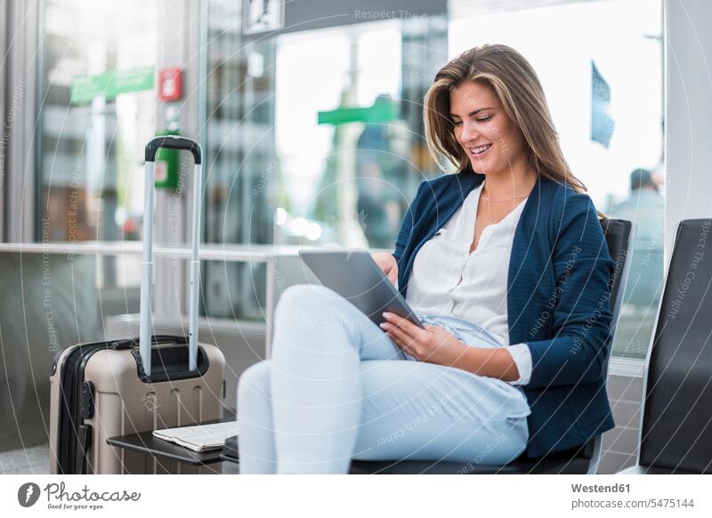 Junge Geschäftsfrau mit Gepäck sitzt mit Tablette im Wartebereich Tablet Computer Tablet-PC Tablet PC iPad Tablet-Computer Geschäftsfrauen Businesswomen