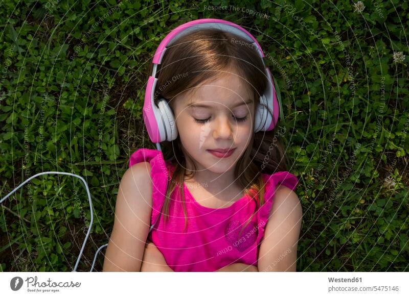 Porträt eines Mädchens, das auf einer Wiese liegt und mit rosa Kopfhörern Musik hört hören hoeren liegen liegend Wiesen Portrait Porträts Portraits Kopfhoerer