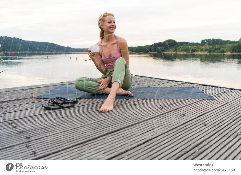Junge Frau trinkt Kaffee aus Tasse an einem See Handtuecher Handtücher entspannen relaxen sitzend sitzt früh Frühe Morgen sommerlich Sommerzeit entspanntheit