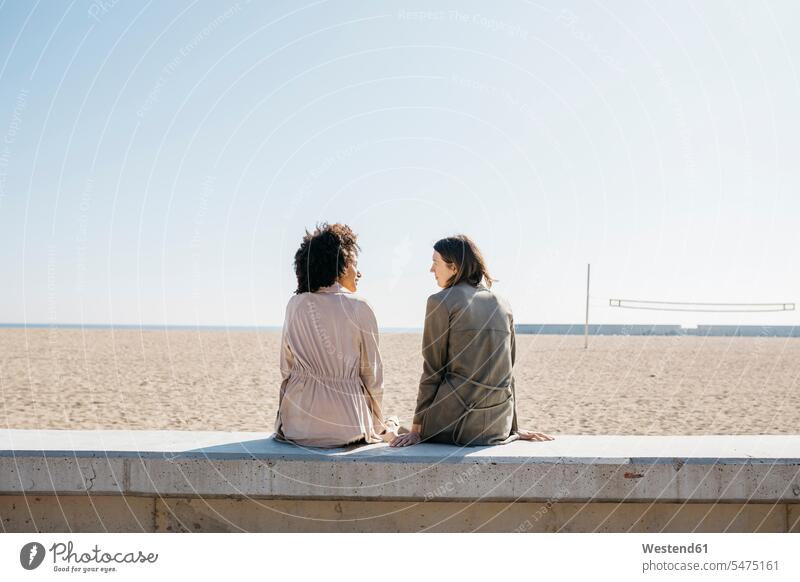 Rückenansicht von zwei Freunden, die auf der Promenade sitzen und ihre Freizeit genießen Freundinnen Frau weiblich Frauen Promenaden Muße geniessen Genuss