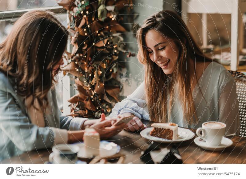 Zwei glückliche junge Frauen mit Handy Treffen in einem Café Spanien modisch Instant Messaging Messenger Tisch Tische Kuchen Freizeit Muße sitzen sitzend sitzt