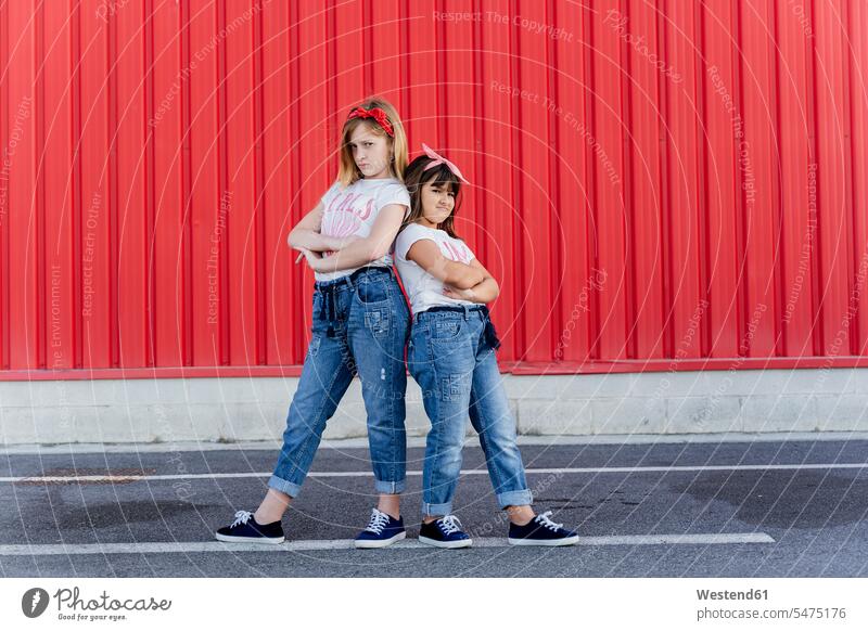 Zwei Schwestern stehen vor einer roten Wand Freunde Kameradschaft Freundin Hosen Jeanshose T-Shirts freuen Glück glücklich sein glücklichsein innig nah roter