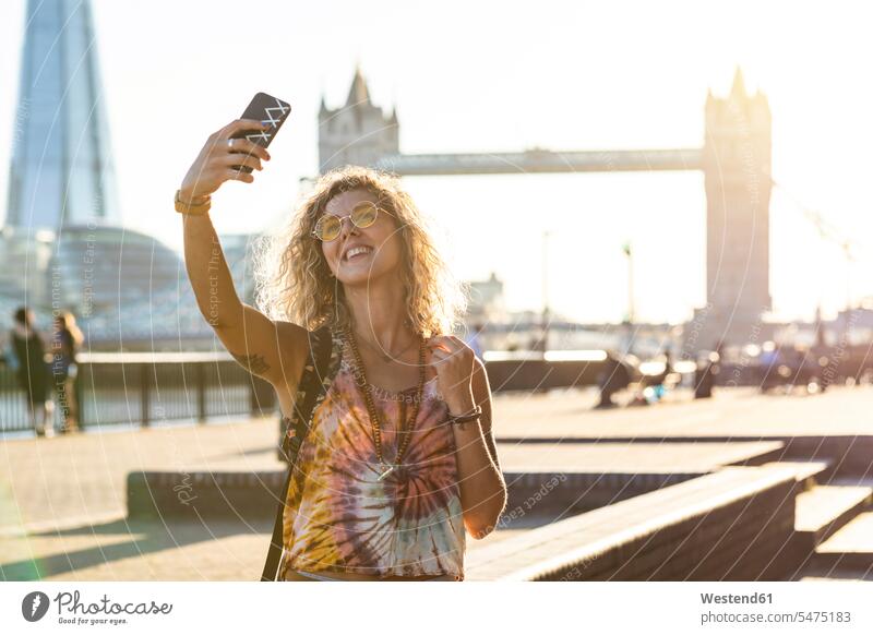 Großbritannien, London, lächelnde junge Frau, die ein Selfie mit der Tower Bridge im Hintergrund macht Selfies weiblich Frauen Brücke Bruecken Brücken glücklich