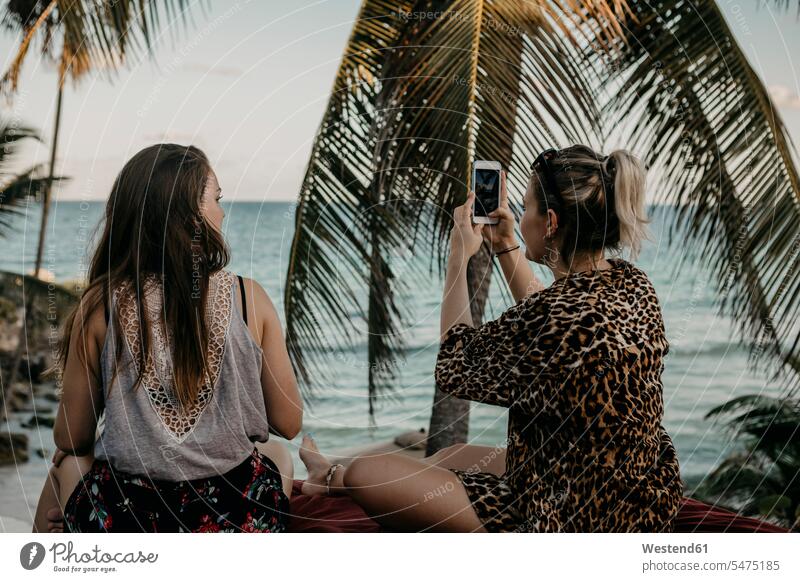 Mexiko, Quintana Roo, Tulum, zwei junge Frauen mit Handy entspannen am Strand Meer Meere Touristin Smartphone iPhone Smartphones Matratze steinig Erholung