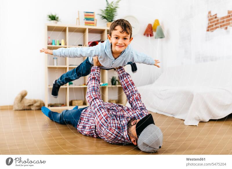 Vater liegt auf dem Boden, hält den Sohn in der Luft und tut so, als würde er fliegen Couch Couches Liege Sofas Ablage Regale fliegend freuen Glück