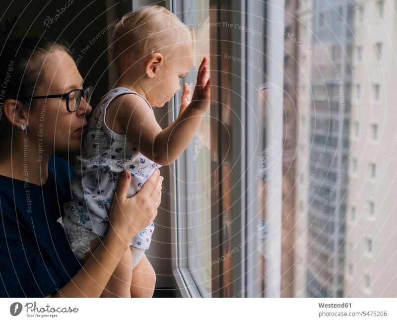 Mutter hält einen kleinen Jungen, der zu Hause durchs Fenster schaut Farbaufnahme Farbe Farbfoto Farbphoto Innenaufnahme Innenaufnahmen innen drinnen Tag