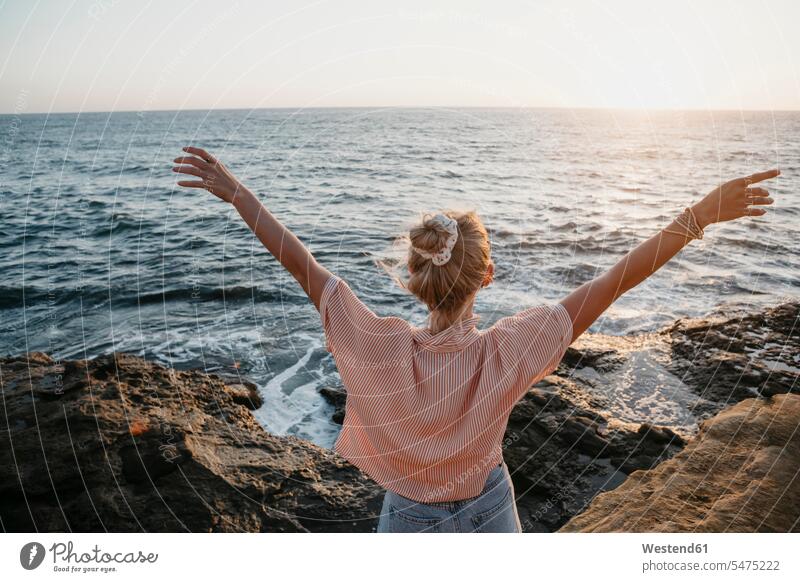 Rückansicht einer jungen Frau am Meer mit erhobenen Armen, Sunset Cliffs, San Diego, Kalifornien, USA Touristen abends Jahreszeiten sommerlich Sommerzeit