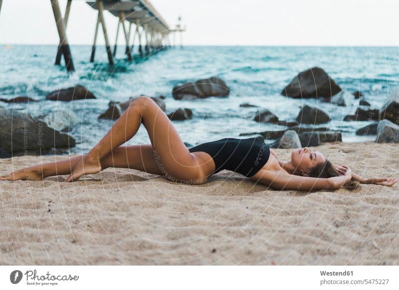 Schöne junge Frau trägt Badeanzug am Strand liegen Badeanzuege Badeanzüge Beach Straende Strände Beaches weiblich Frauen liegend liegt schön Badekleidung