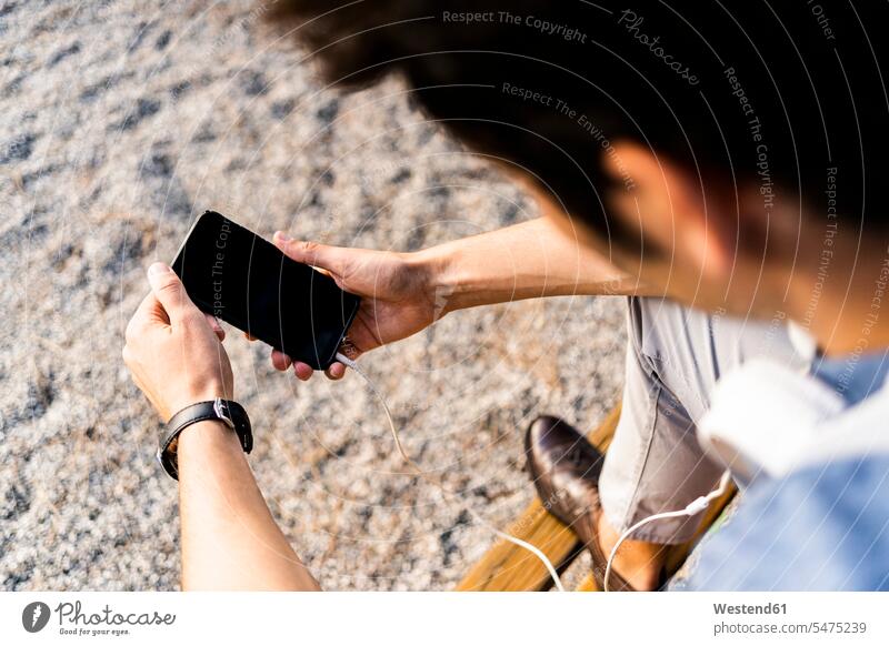 Nahaufnahme eines Mannes, der mit seinem Smartphone auf einer Parkbank sitzt Leute Menschen People Person Personen Europäisch Kaukasier kaukasisch 1 Ein
