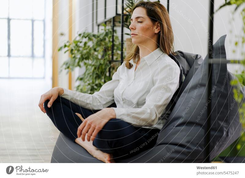 Frau praktiziert Yoga, während sie im Büro auf einem Sitzsack sitzt Farbaufnahme Farbe Farbfoto Farbphoto Innenaufnahme Innenaufnahmen innen drinnen Tag