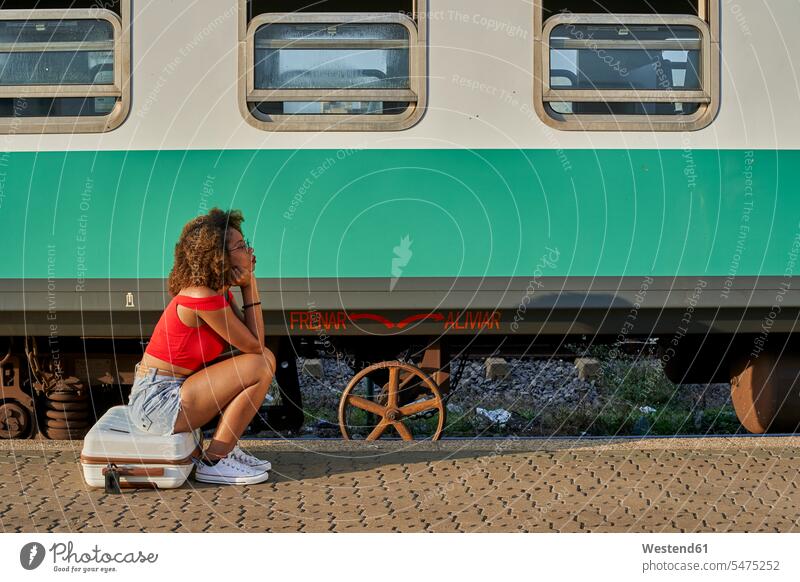 Frau mit Koffer sitzend auf dem Bahnhof rot rote roter rotes Locken lockiges Haar gelockte Haare gelocktes Haar warten Passagierzug Passagierzüge Personenzug
