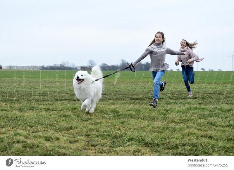 Zwei Mädchen laufen auf einer Wiese mit Hund Spaß haben Spass Späße spassig Spässe spaßig Wiesen weiblich rennen Hunde Kind Kinder Kids Mensch Menschen Leute