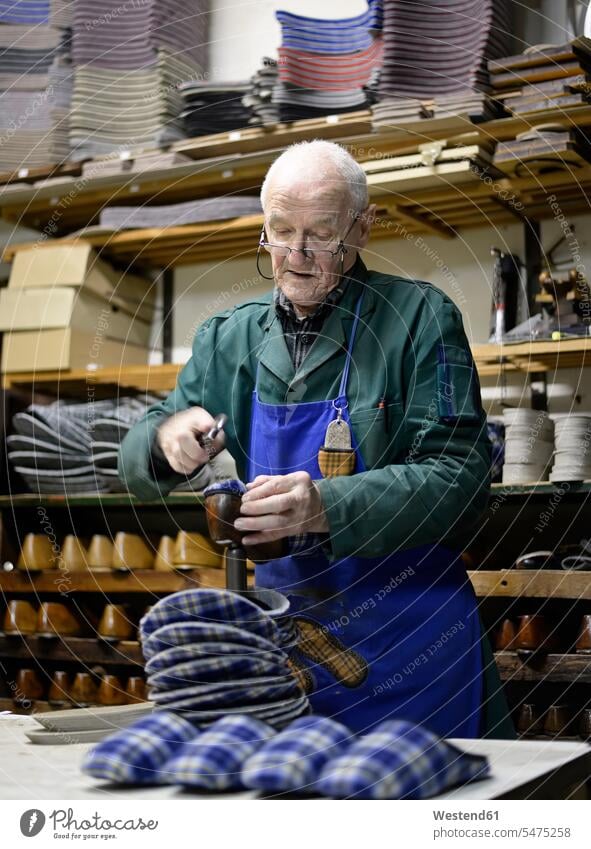 Senior-Schuhmacher bei der Arbeit an Hausschuhen in der Werkstatt Schuster Werkstätte Werkstaette Werkstaetten Werkstätten arbeiten Puschen Pantoffeln