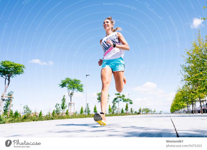 Mittlere erwachsene Frau joggt auf der Straße vor blauem Himmel Farbaufnahme Farbe Farbfoto Farbphoto Spanien Außenaufnahme außen draußen im Freien Tag