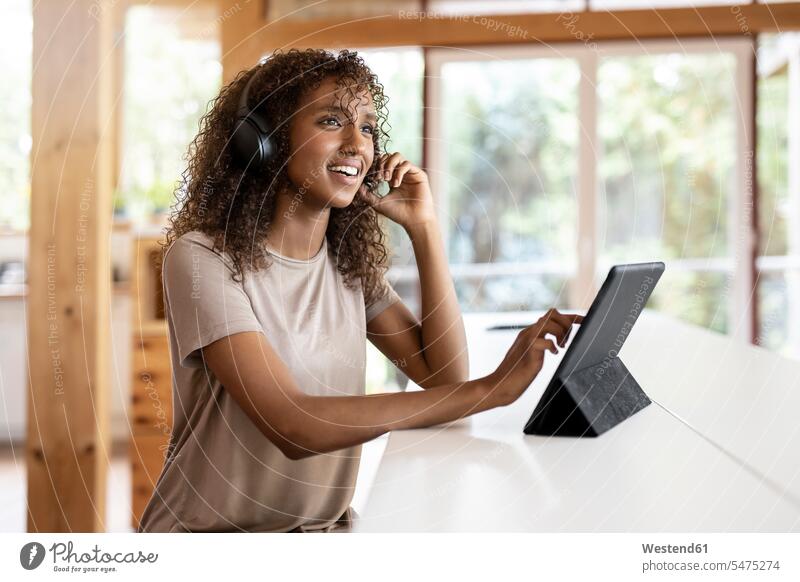 Geschäftsfrau mit digitalem Tablet spricht über Kopfhörer, während sie zu Hause sitzt Farbaufnahme Farbe Farbfoto Farbphoto Innenaufnahme Innenaufnahmen innen