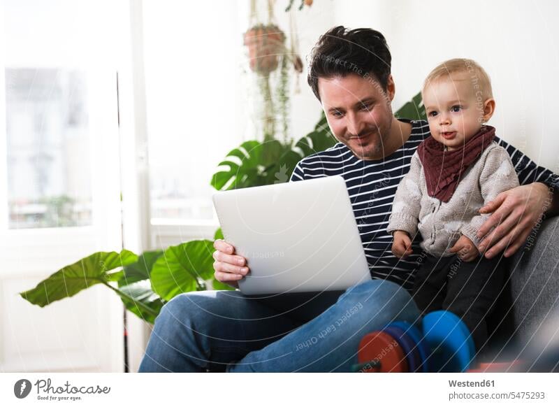 vater sitzt mit seiner kleinen Tochter auf dem Sofa und benutzt einen Laptop Laptop benutzen Laptop benützen Vater Papas Väter Vati Vatis Papis Töchter sitzen
