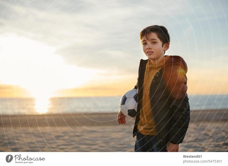 Porträt eines Jungen, der bei Sonnenuntergang am Strand Fußball hält Beach Straende Strände Beaches Fußbälle Fussball halten Portrait Porträts Portraits