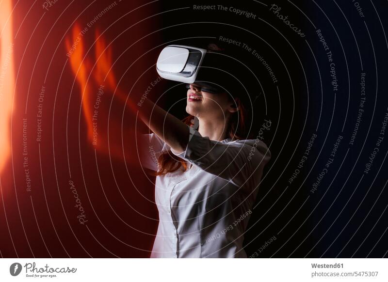 Junge Frau gestikuliert, während sie eine VR-Brille auf schwarzem Hintergrund trägt Farbaufnahme Farbe Farbfoto Farbphoto Studioaufnahme Studioaufnahmen